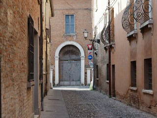 Fototapeta na wymiar Ferrara, Italy. Cobbled street in the old town. There is an old house with a large wooden door.