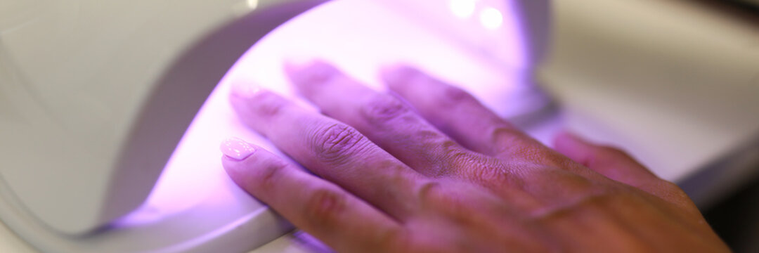 Woman dries her nails in a professional UV lamp