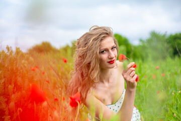 A young long-haired girl enjoys the colors of nature on a blooming poppy field on a hot summer day