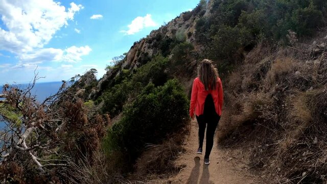 Woman walking through path against Calpe coast in the penon the ifach. Tourists visit Calp and Penyal d'Ifac Natural Park. View of Calp coast from a path above sea level