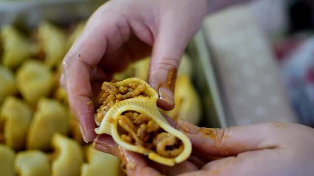 Preparation of homemade lumaconi filled in with tomato sauce and minced meat. Close up of man's hands stuffing homemade Italian pasta recipe