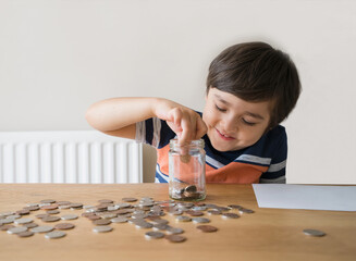 School Kid putting money coins into clear jar, Child counting his saving money, Young boy holding...