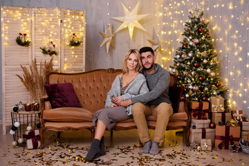 Obraz premium winter holidays and relationship concept - happy young couple in living room with decorated Christmas tree