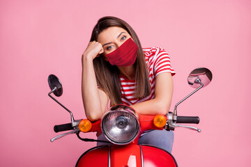Portrait of girl sitting on moped wearing red face mask isolated over pink pastel color background