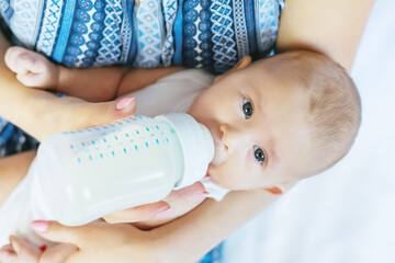 Mom feeds the baby with a bottle. Selective focus.