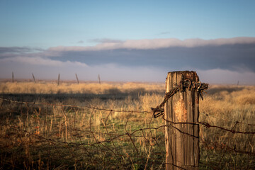 Fence post with barbed wire in valley with storm