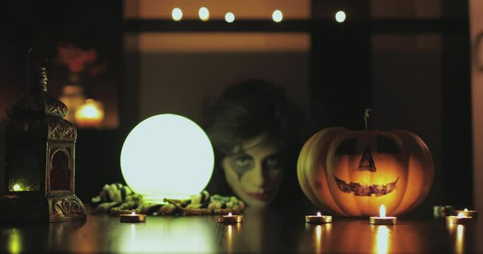 Female with scary halloween mask with pumpkin and crystal magic ball. 