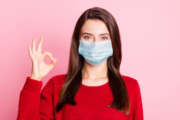 Photo of young lovely girl raise arm show okey look camera wear mask red sweater isolated pink color background