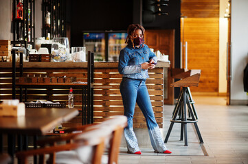 Stylish african american woman with dreadlocks afro hair, wear jeans jacket and face protect  mask...