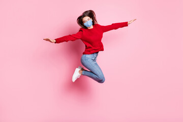 Fototapeta na wymiar Full length portrait of girl jumping high wearing mask casual clothes keeping hands like plane isolated on pink color background