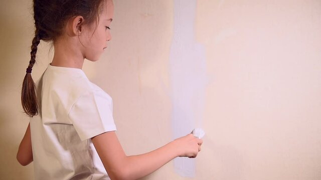 7-year-old girl in a gray t-shirt paints the wall gray with a paint brush