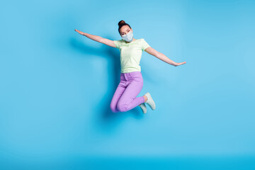 Fototapeta na wymiar Full length photo of young girl jumping high keeping hands like plane wear mask isolated on vibrant blue color background