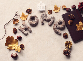 Composition with homemade cookies in shape of letters HOME, brown notebook, golden leaves, chestnuts and cones. Copy space.