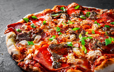 Pizza with Mozzarella cheese, salami, chicken meat, beef, ham, Tomato sauce, pepper, spices. Italian pizza on Dark grey black slate background