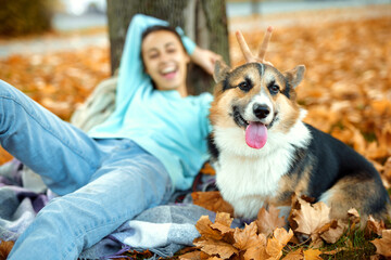 Funny Welsh Corgi dog with woman owner at autumn park having fun, spending time together, colorful fallen leaves on background