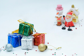 Focus at colorful gift boxes pile with blurred Santa Claus doll and Christmas decorations on white background