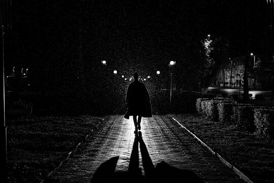 Dramatic Silhouette Of A Man In A Hat And Raincoat Walking Through The City At Night