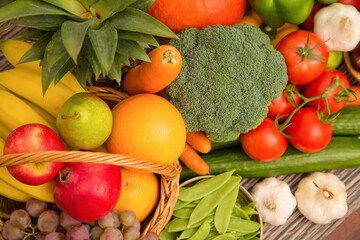 Naklejka na ściany i meble Group vegetables and Fruits Apples, grapes, oranges, and bananas in the wooden basket with carrots, tomatoes, guava, chili, eggplant, and salad on the table.Healthy food concept