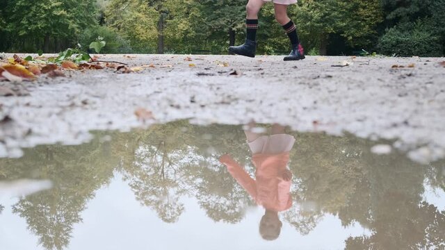 reflection of a cheerful dancing little girl on a puddle of water on an autumn morning