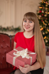 Portrait of a beautiful blonde girl with a Christmas gift near the Christmas tree