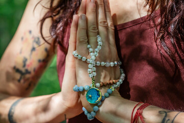 Female hands doing namaste mudra yoga practice in forest with mala necklace