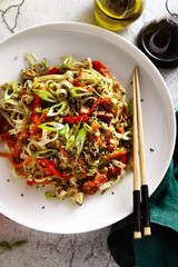 vegan pad thai rice pasta with vegetables and tofu on gray concrete background with soy sauce and sesame oil