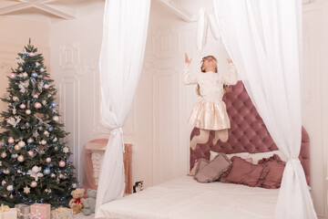 Fototapeta na wymiar The girl does not want to sleep on Christmas night and jumps on the bed