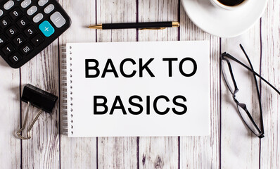The word BACK TO BASICS is written in a white notepad near a calculator, coffee, glasses and a pen....