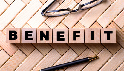 The word BENEFIT is written on wooden cubes on a wooden background next to a pen and glasses.