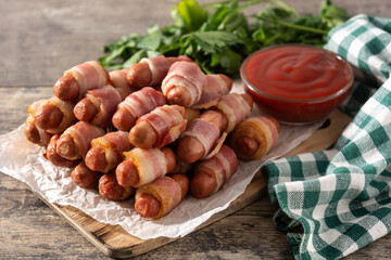 Pig in blankets. Sausages wrapped in smoked bacon on wooden table	