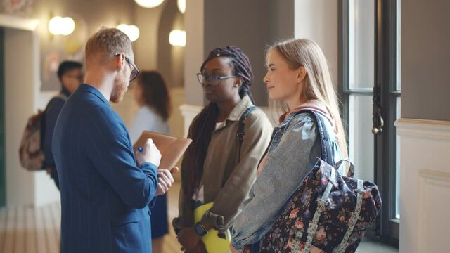 Young male professor discussing thesis with diverse female students in corridor
