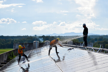 The workers of the photovoltaic company are spreading water and washing the surface of the solar...
