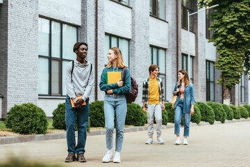 Obraz premium Selective focus of african american teenager with book walking near friend on urban street