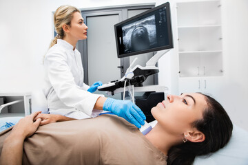 Woman endocrinologist making ultrasonography to a female patient in an ultrasound office. Ultrasound diagnostics of the thyroid gland.