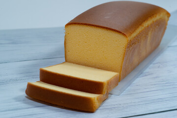 Homemade sliced butter cake on white wooden background.