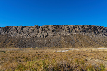 The road leads to the mountains. Mountain highway. Asphalt texture. Country highway. Mountains and hills in autumn. Mountain plants in autumn. Plants on the roadside. Dry yellow grass. Blue sky