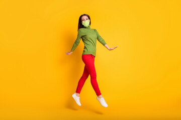 Fototapeta na wymiar Full size profile photo of funny lady jump up walking wear mask green pullover sneakers trousers isolated yellow color background