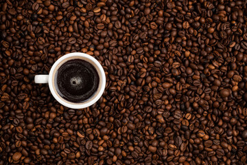 cup full of black coffee over a background of coffee beans