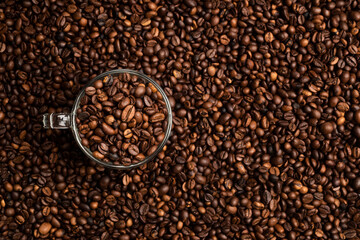 glass cup full of coffee beans over a background of coffee beans