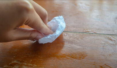 Hand using tissue paper to
wipe wooden table .