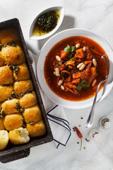 Ukrainian soup borsch with mushrooms and white beans and pampushki buns on a marble table