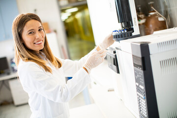 Female scientist in a white lab coat putting vial with a sample for an analysis on a gas...