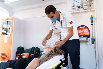 Male paramedic with face mask helping a patient with respirator in ambulance during pandemic