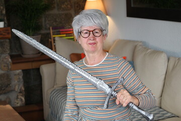 Senior geek holding a sword at home 