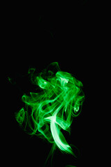 Whimsical curls and shapes of green smoke on a dark background. Streaming smoke from a burning incense stick.