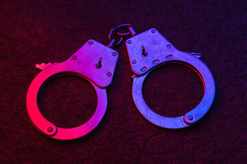 Handcuffs on a dark background, illuminated by flashing lights of a police car, close-up