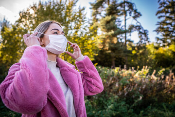 A young woman with a protective face mask is on a walk in nature and she is thinking about when the quarantine ends - topic of corona virus - COVID 19.