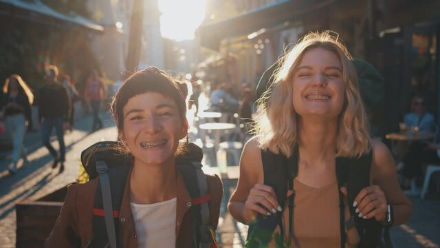 Couple portrait of funny caucasian two travel women with backpacks smiling into camera showing teeth with braces having fun laughing. Tourists.