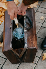 Hands take out magnifying glass from leather carpetbag on autumn alley