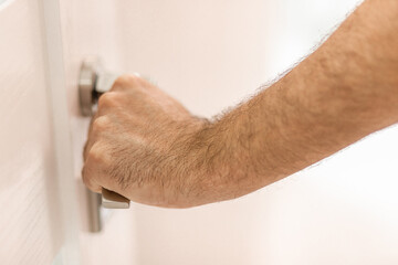 Photo of a male hand holding a metal handle of a white door.